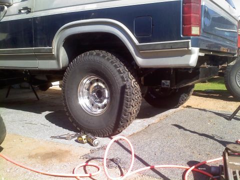 1986 Ford Bronco - The rear of a 1986 Ford Bronco is visible, large tires and a dark blue and silver paint job, with another vehicle partially seen in the bac…