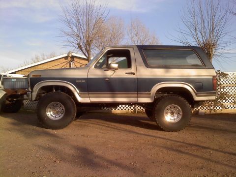 1986 Ford Bronco - This lifted Ford Bronco features a two-tone paint scheme and is parked outdoors on a dirt lot.