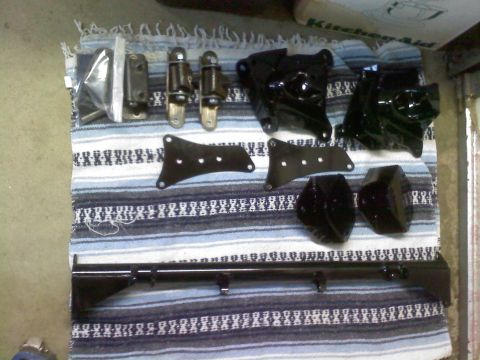 1986 Ford Bronco - A collection of black automotive parts, including brackets and hinges, are displayed on a striped blanket.