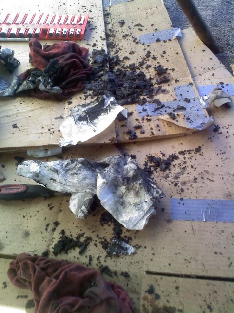 1986 Ford Bronco - A messy scene of automotive repair with greasy rags and tools scattered on cardboard.