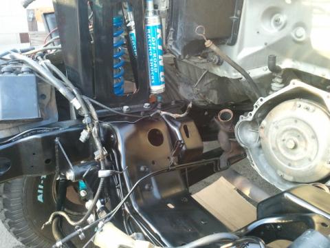 1986 Ford Bronco - Close-up view of vehicle chassis and engine parts, including blue racing shocks and visible wiring.