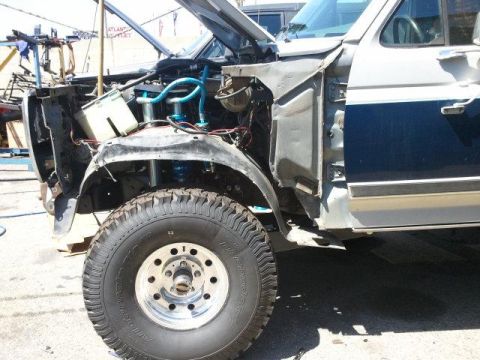 1986 Ford Bronco - Front end of a 1986 Ford Bronco undergoing repairs, with hood open and fender removed.