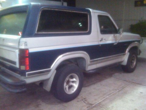 1986 Ford Bronco - This 1986 Ford Bronco features a distinctive blue and white two-tone paint scheme and is shown from the rear three-quarter angle.