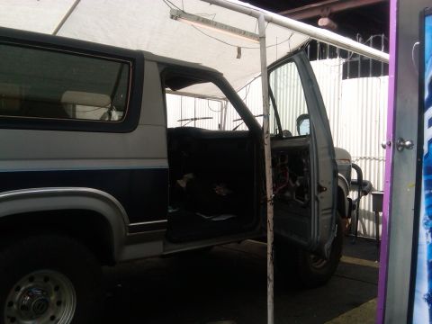 1986 Ford Bronco - The driver's door is open on this 1986 Ford Bronco, revealing the interior and some of the engine components.