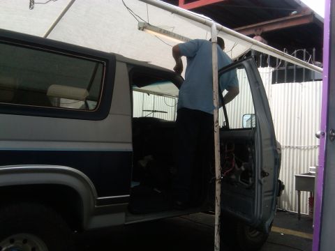 1986 Ford Bronco - A person is working on the interior of a two-tone gray and blue Ford Bronco, with the driver's door removed.