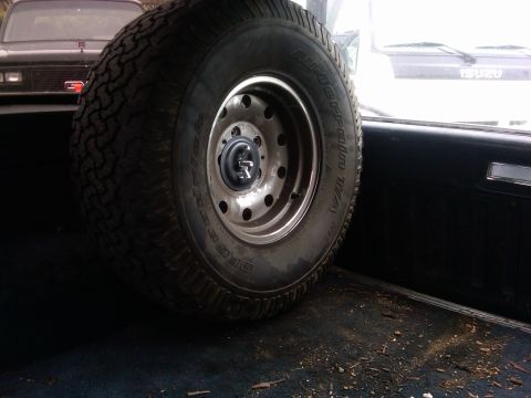 1986 Ford Bronco - A spare tire is secured inside the cargo area of a vehicle, with other vehicles visible through the windows.