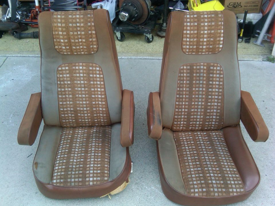 Two brown and tan plaid bucket seats with armrests, showing some wear