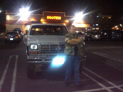 1986 Ford Bronco - A silver 1986 Ford Bronco is parked in front of a Hooters restaurant at night, with a man standing in front of the vehicle.