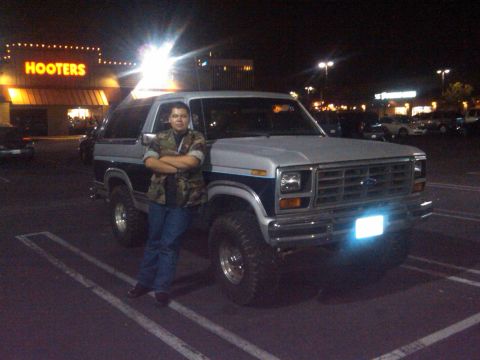 1986 Ford Bronco - A person poses with a 1986 Ford Bronco in a parking lot at night, with a Hooters restaurant in the background.