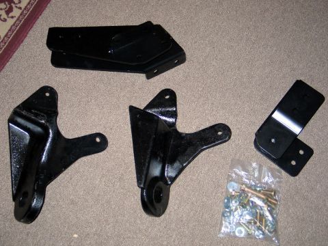 1995 Ford Bronco - Several black metal lift kit components and a bag of hardware are laid out on a carpeted floor.