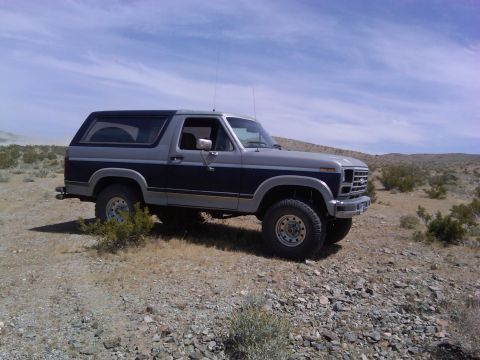 1986 Ford Bronco - This two-tone Ford Bronco is parked on a rocky, arid terrain under a partly cloudy sky.