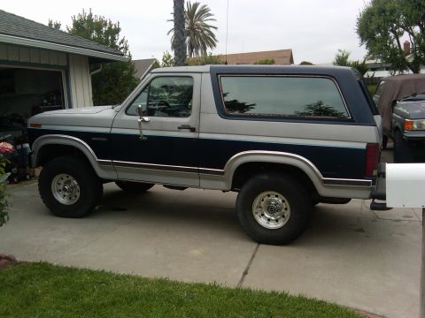 1986 Ford Bronco - This Ford Bronco features a two-tone paint scheme with a dark blue stripe separating the gray upper and lower sections.