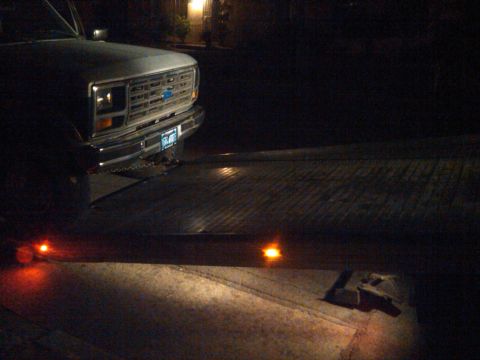1986 Ford Bronco - A truck's front end is visible, a Chevrolet emblem and a license plate, illuminated by amber lights on a flatbed trailer.