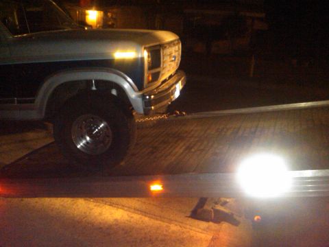1986 Ford Bronco - A two-tone pickup truck, likely from the 1980s, is being loaded onto a flatbed trailer at night.