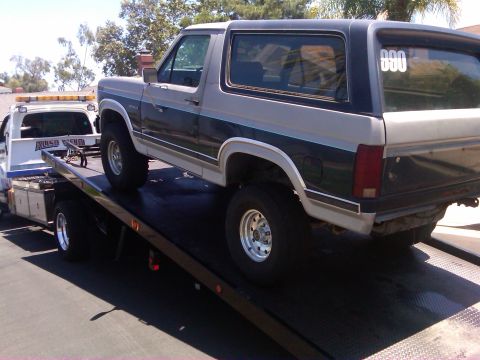 1986 Ford Bronco - A Ford Bronco is loaded onto a tow truck, with a tow truck visible behind it.