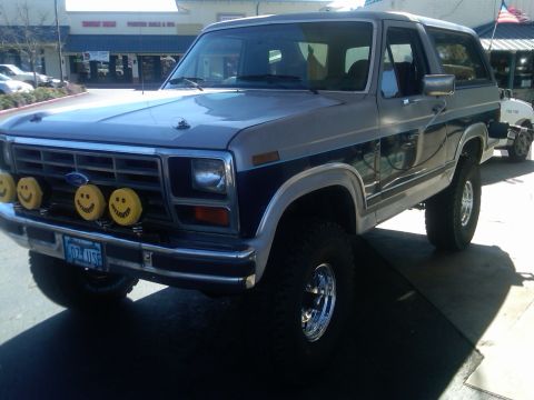 1986 Ford Bronco - This two-tone Ford Bronco has a custom grille with four yellow smiley face lights and aftermarket wheels.