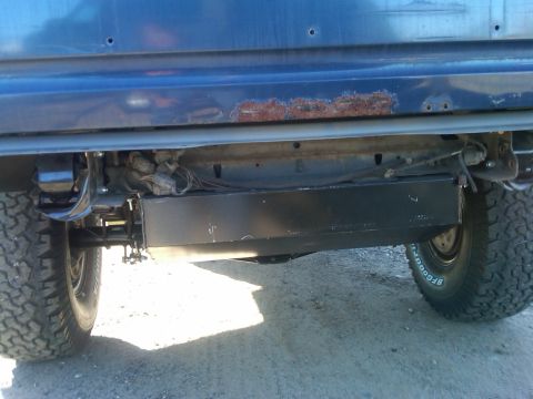 1986 Ford Bronco - The rear undercarriage of a dark blue SUV shows rust on the body panel and BFGoodrich tires.