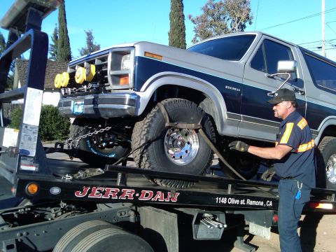 1986 Ford Bronco - A tow truck operator secures a two-tone Ford Bronco for transport.