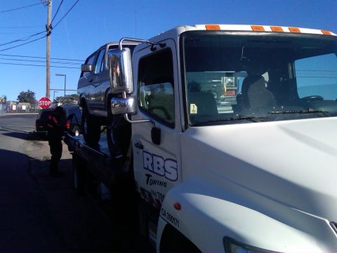 1986 Ford Bronco - A gray Ford Bronco is loaded onto a white tow truck on a sunny day.