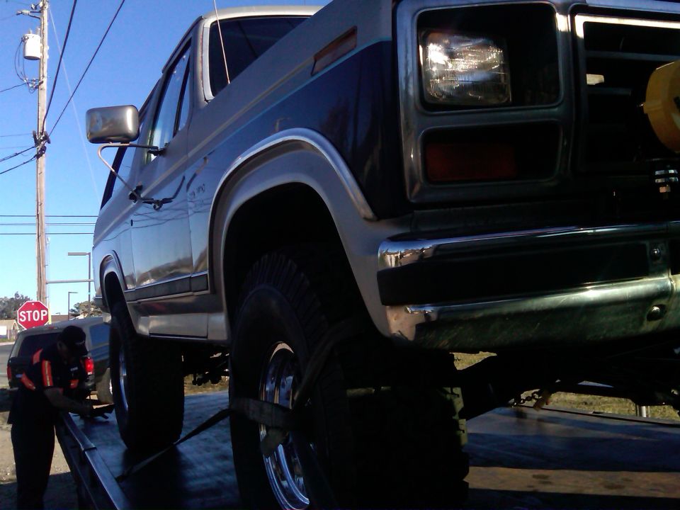 Ford Bronco on tow truck, front quarter view. A person in a safety vest is securing it