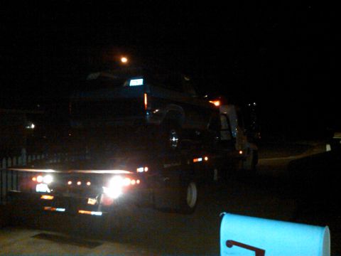 1986 Ford Bronco - A tow truck transports a vehicle at night, illuminated by its own lights and a distant streetlamp.