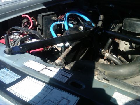 1986 Ford Bronco - Close-up view of the engine compartment, showing various hoses, wiring, and the battery.