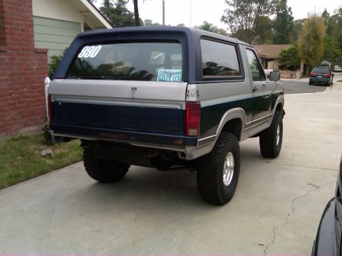 1986 Ford Bronco - This lifted 1986 Ford Bronco is parked in a driveway, showing its rear end and custom off-road modifications.