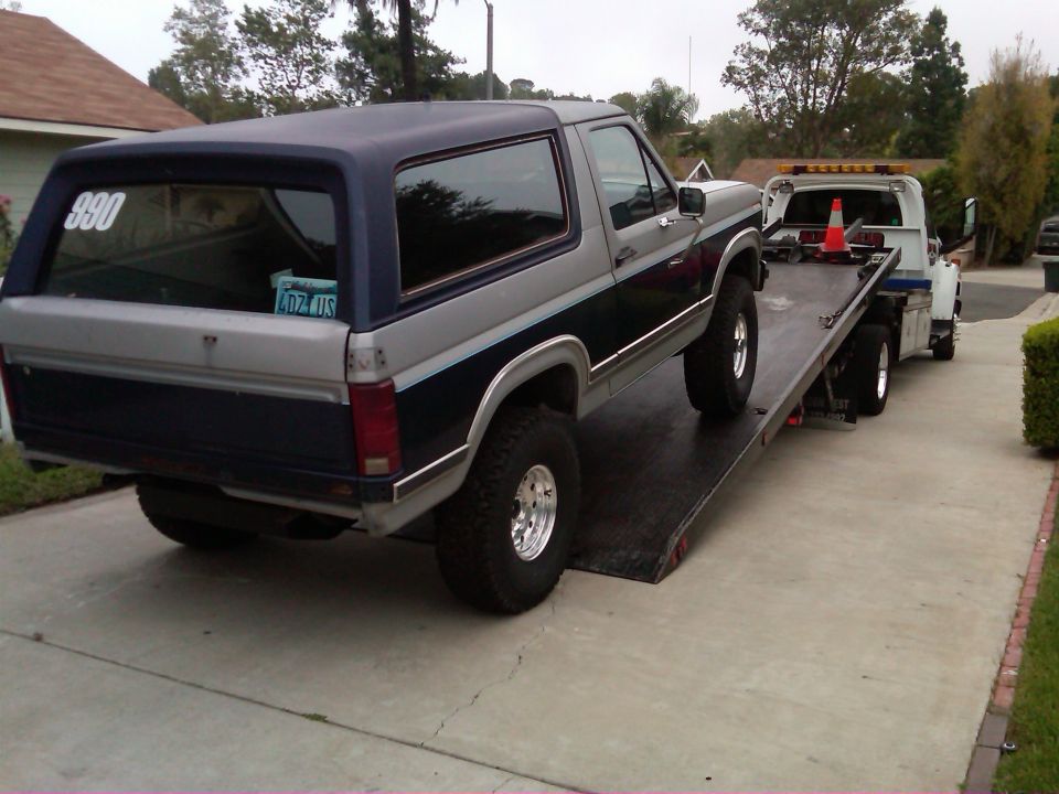 1986 Ford Bronco being loaded onto a tow truck, rear view. License plate visible