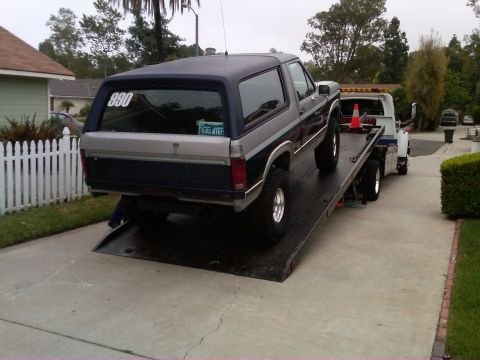 1986 Ford Bronco - A Ford Bronco is loaded onto a tow truck, with a license plate visible in the rear window.
