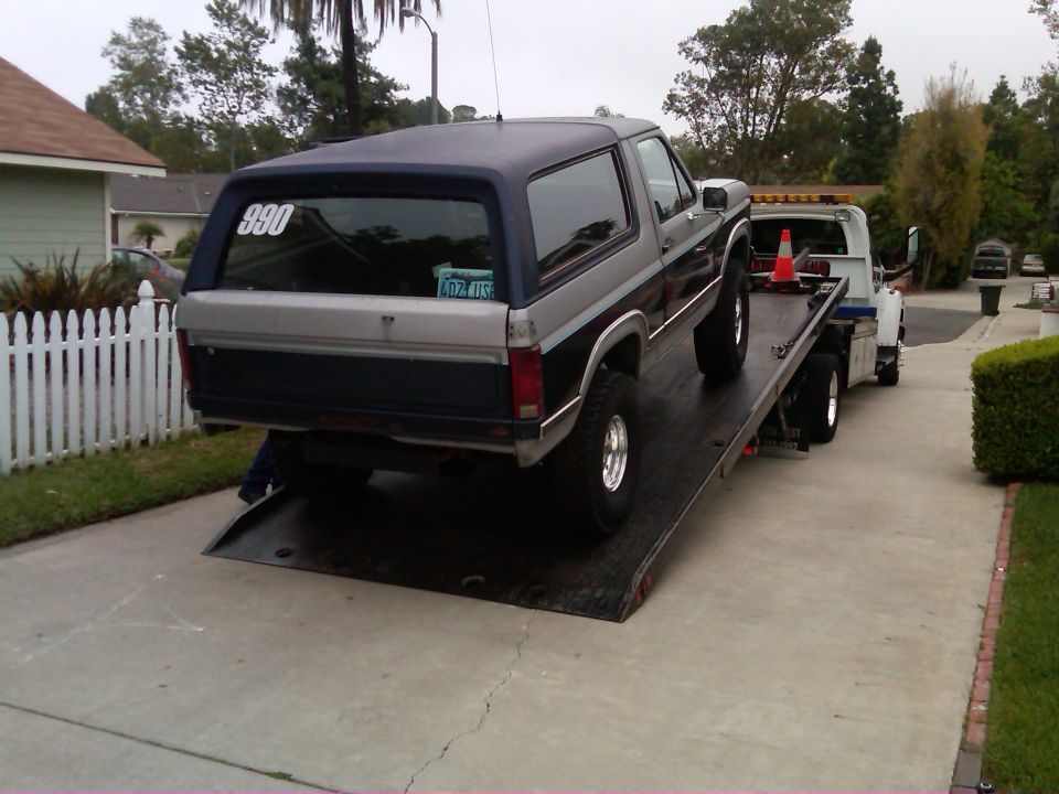 Two-tone gray and blue Ford Bronco being towed on a flatbed truck