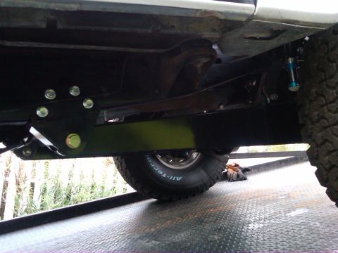 1986 Ford Bronco - The underside of a 1986 Ford Bronco reveals custom suspension parts and BFGoodrich All-Terrain tires, indicating off-road enhancements.
