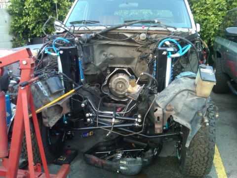 1986 Ford Bronco - The front end of an SUV is disassembled, revealing the engine and transmission area, with repair equipment present.