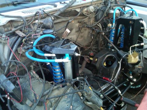 1986 Ford Bronco - The engine bay shows a complex setup with custom blue suspension components and extensive wiring, suggesting significant modifications.
