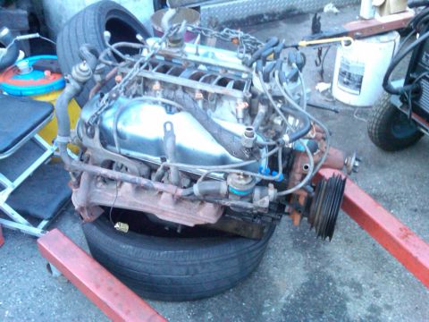 1986 Ford Bronco - An engine, likely removed from a vehicle, is supported by an engine stand and a tire.