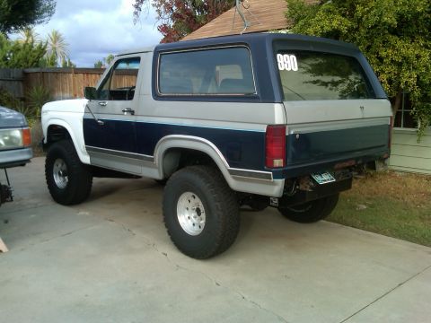 1986 Ford Bronco - Rear view of a lifted 1986 Ford Bronco with off-road tires and two-tone paint scheme.