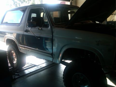 1986 Ford Bronco - This two-tone Ford Bronco is on a lift with its hood open, showing the engine bay.