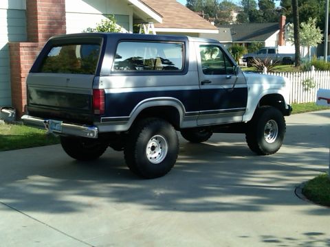 1986 Ford Bronco - This two-tone Ford Bronco is parked in a residential driveway, showing its side and rear profile.