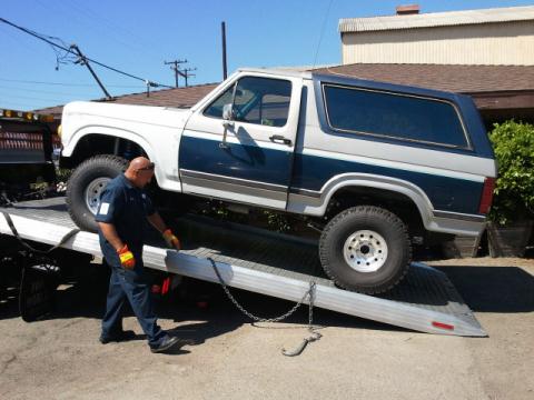 1986 Ford Bronco - A man secures a two-tone Ford Bronco onto a flatbed tow truck.