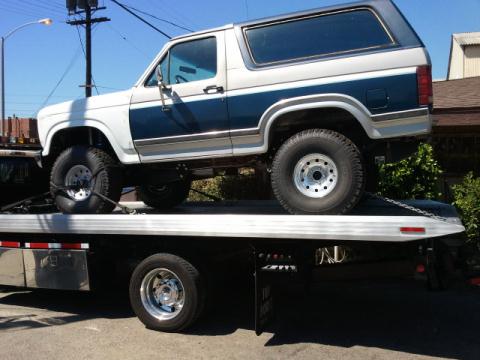 1986 Ford Bronco - A white and blue Ford Bronco is loaded onto a flatbed tow truck.