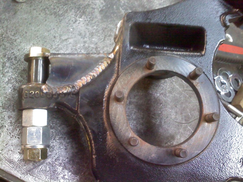 Black metal suspension component with visible welds and bolt assembly, showing a circular flange with studs