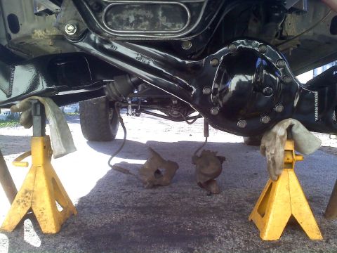 1986 Ford Bronco - The rear axle assembly of a vehicle is elevated on jack stands, with brake calipers detached and lying on the ground.