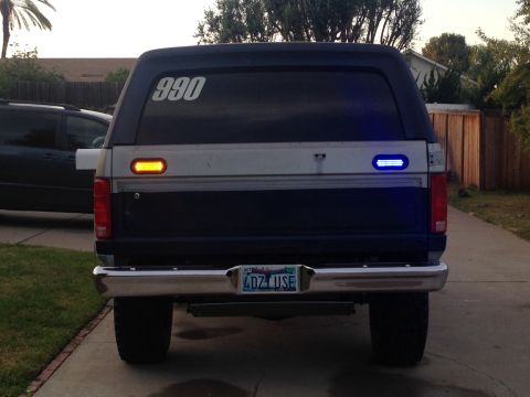 1986 Ford Bronco - Rear view of a Ford Bronco, showing its taillights and license plate. A second vehicle is visible to the left.