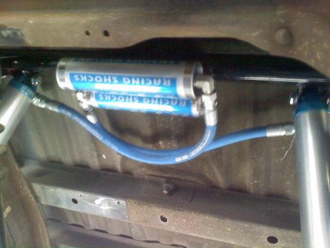 1986 Ford Bronco - The underside of a vehicle displays a pair of blue racing shocks and their associated plumbing.