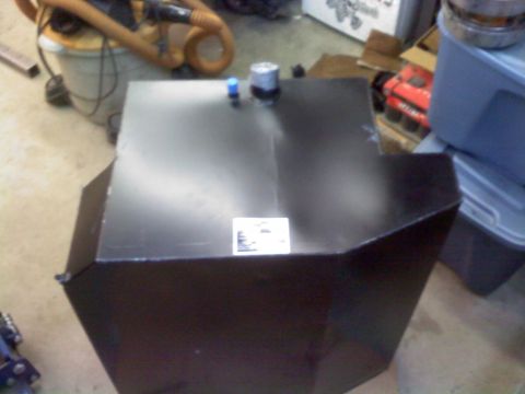 1986 Ford Bronco - A black aftermarket fuel tank is shown with a label on its surface and two fittings on top.