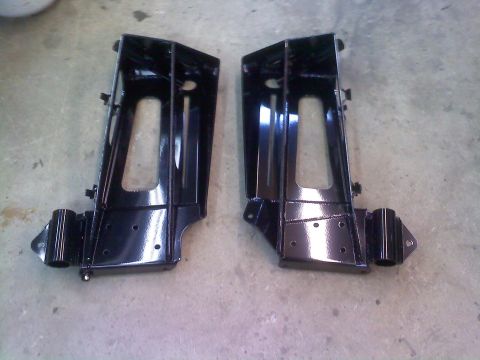 1986 Ford Bronco - Two black metal brackets are shown on a concrete surface, likely automotive parts.
