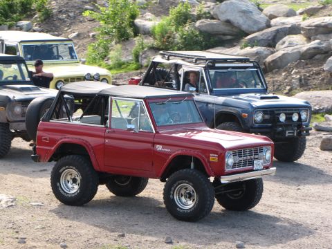 1979 Ford Bronco - Several Ford Broncos are gathered off-road, with a red Bronco in the foreground.