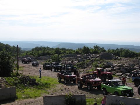 1979 Ford Bronco - A group of Ford Broncos and other off-road vehicles gathered on a dirt path with a mountainous backdrop.