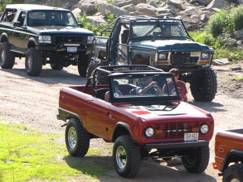 1979 Ford Bronco - Several modified off-road vehicles are lined up on a dirt path, with a red Ford Bronco in the foreground.