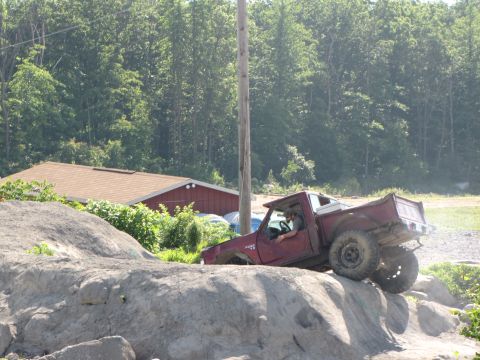 1979 Ford Bronco - This pickup truck is navigating a challenging rocky terrain, with trees and a building in the background.