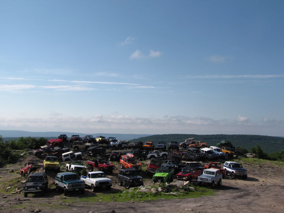 Lots of SUVs and trucks parked on a rocky hill under a blue sky